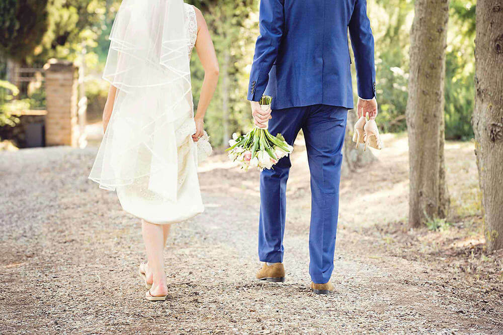 A bride and groom walking off in Tuscany. The groom is carrying the brides shoes and bouquet.