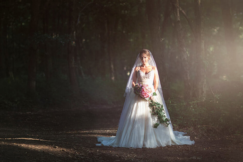 A stunning Bride poses in the sunlight in the woods.